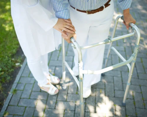 close-up-of-clinician-hand-on-that-of-disabled-woman-with-walking-frame-SBI-300908526