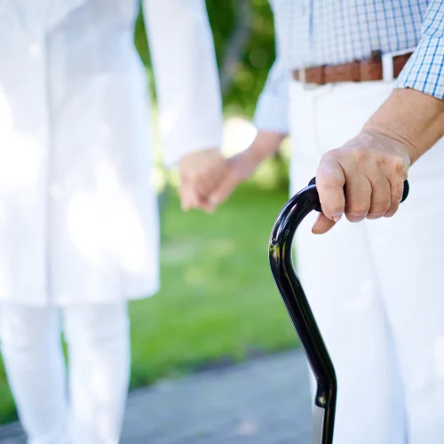 close-up-of-disabled-female-hand-holding-cane-with-her-doctor-walking-near-by-SBI-300734433